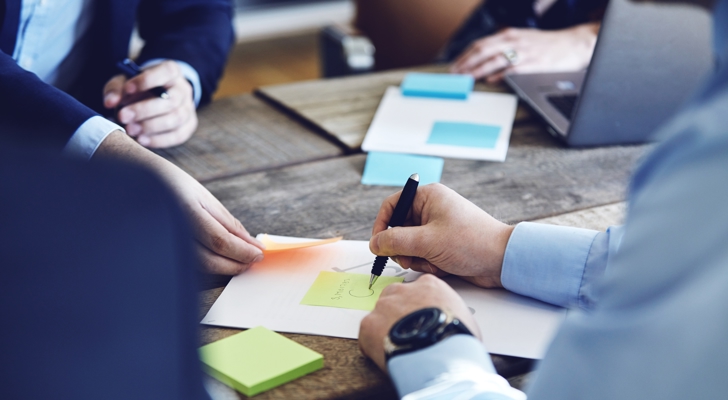 Møde mellem fire personer hvor der bliver skrevet på papir og post-it