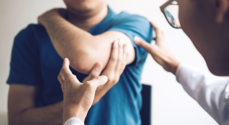 Læge der kigger på en arm eller albue ved en erstatning