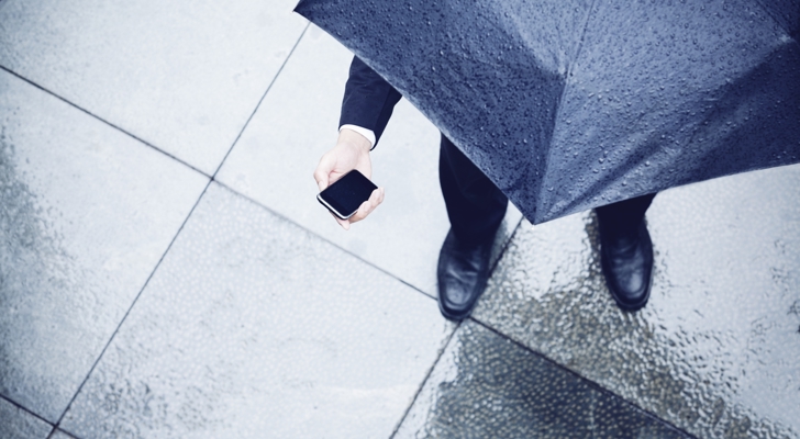 Person står under paraply med telefon i hånden