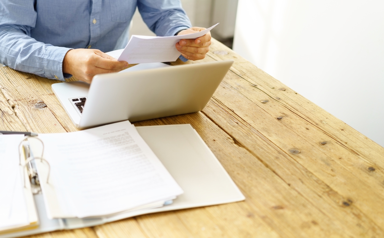 Mand arbejder ved computer og gennemgår papirdokumenter