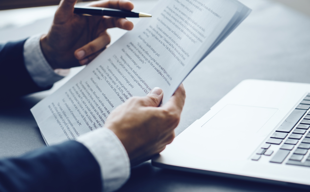 Person gennemgår kontrakt med laptop foran sig